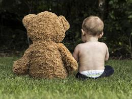 Ein Baby sitzt mit seinem Teddy auf einer Wiese