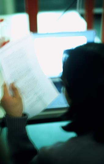 Studierender vor einem Computerbildschirm mit einem Blatt Papier in der Hand.