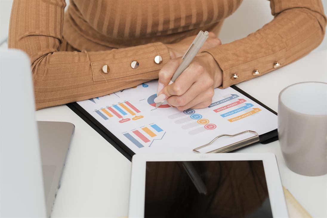 Hand einer Frau* schreibt etwas auf ein Blatt, auf dem Graphen abgebildet sind