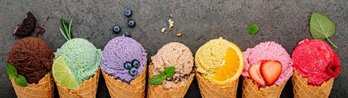 Verschiedene von Eissorten in Waffeln: Heidelbeere, Limette, Pistazie, Mandel, Orange, Schokolade, Vanille und Kaffee vor einem dunklen Stein-Hintergrund angerichtet. 