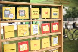 Abgebildet ist ein Holzrahmen mit vielen drehbaren, flachen Holzquadraten drauf. Die Quadrate bilden gelb-rote Illustrationen ab.