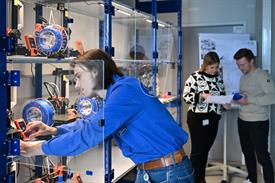 Student in blauem Hemd an einem Regal mit 3-D-Druckern hinter Glaswänden