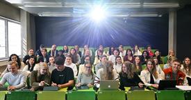 Viele Studierende in einem Hörsaal mit grünen Sitzen und einem Beamer in das Bild strahlt