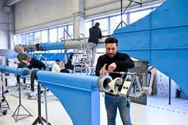 Sechs Männer stehen an großen Rohren mit blau gestrichenen Elementen