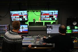 Zwei Männer sitzen an einem Regiepult mit vielen Monitoren und hinter einer Scheibe stehen eine Frau und ein Mann vor einem grünen Hintergrund