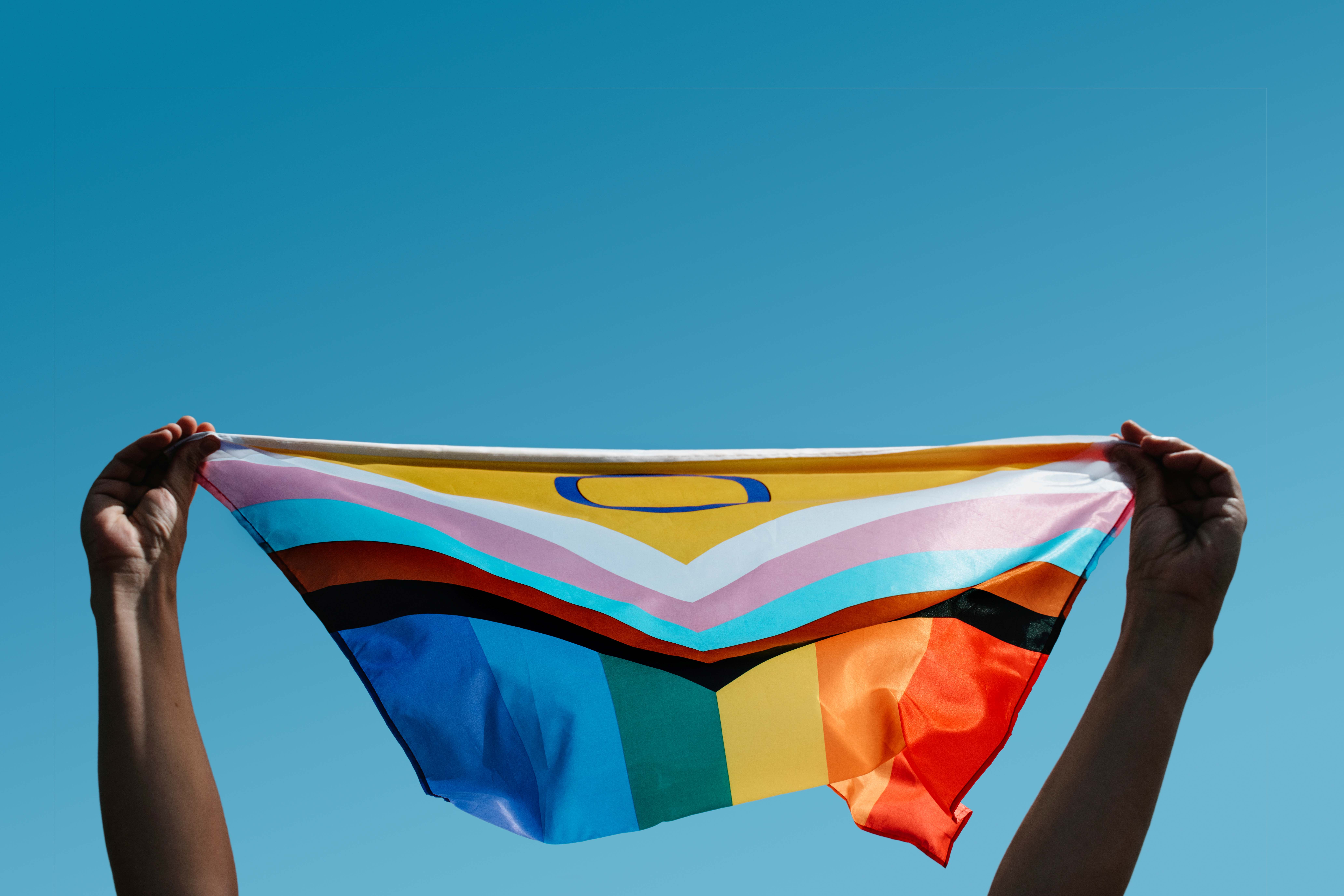 Regenbogenflagge wird festgehalten vor blauem Himmel