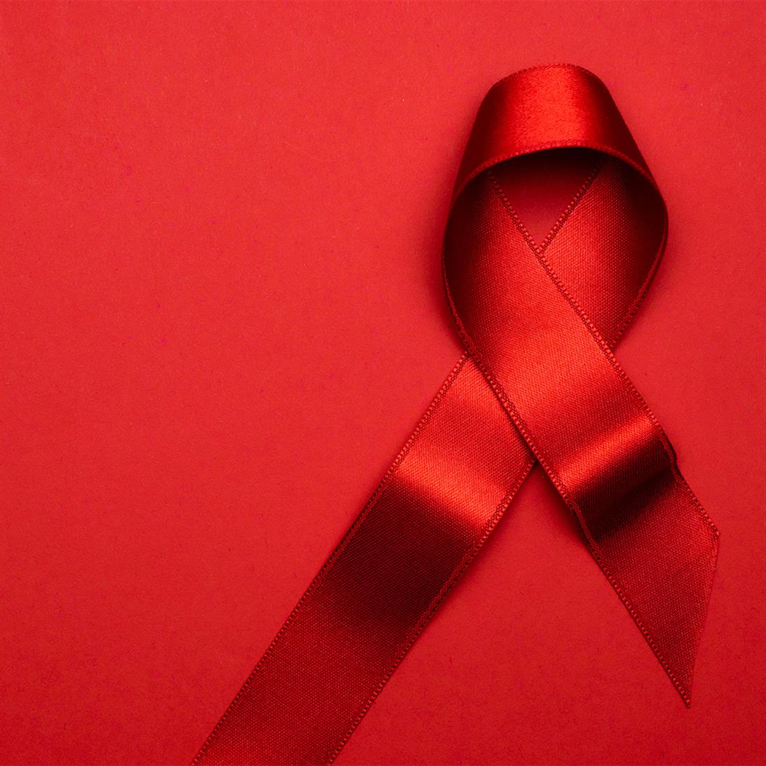 The picture shows the red ribbon as a symbol of solidarity with people infected with HIV and AIDS on a red background.