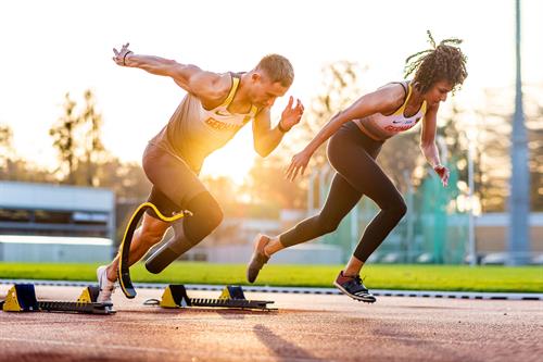 A female runner and a male runner with a prosthetic leg at the starting block