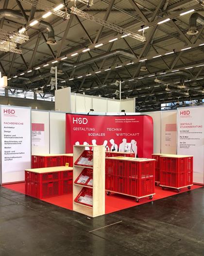 Photo of the HSD booth with exhibition wall, roll-ups, bar tables and brochures.