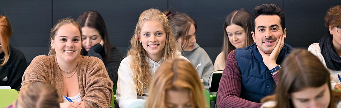 Gruppe weiblicher und männlicher Studierender in einem Hörsaal mit grünen Stühlen