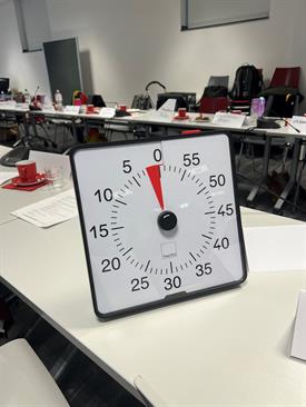 Timer standing on a table. In the background you can see a coffee setting on the table.