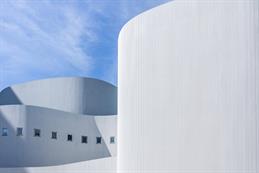 Das Foto zeigt die moderne, weiße Fassade des Düsseldorfer Schauspielhauses. Die geschwungenen, wellenförmigen Linien des Gebäudes wirken elegant und futuristisch, während kleine quadratische Fenster rhythmisch in die Oberfläche eingelassen sind. Der klare blaue Himmel verstärkt den hellen, minimalistischen Eindruck der Architektur.