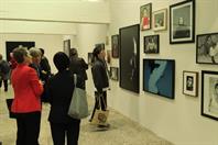 Eine Gruppe von Menschen besucht die Ausstellung und betrachtet verschiedene Fotografien, die an den Wänden ausgestellt sind. Die Besucher*innen sind in ein Gespräch vertieft und betrachten die Kunstwerke aufmerksam. Die Fotografien zeigen Porträts und andere künstlerische Motive in Schwarz-Weiß und Farbe. Der Raum ist schlicht und hell gestaltet, was den Fokus auf die ausgestellten Werke lenkt.