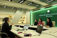 Eine Besprechungsszene im Konferenzraum der Ewha Womans University in Seoul, Korea. Vier Personen sitzen um einen Tisch mit Laptops, Notizen und Wasserflaschen. Eine Person spricht, während die anderen zuhören. Der Raum ist modern eingerichtet mit grünen Akzenten und einem großen Schild an der Wand, das den Namen der Universität trägt.