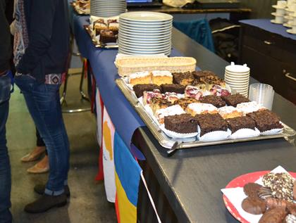 verscheidene Kuchensorten sind auf einer Bar angerichtet, darunter hängen bunte Länderflaggen